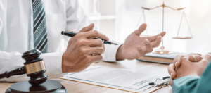 Two people sit at a desk with legal documents, a gavel, and a Tallahassee car accident lawyer.