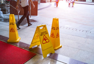 Three yellow caution signs on a tiled floor next to a red carpet in a public area.