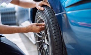 Person checking tire pressure on a blue car using a pressure gauge.
