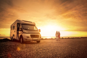 A camper van parked by the beach at sunset with two people standing by the shore.
