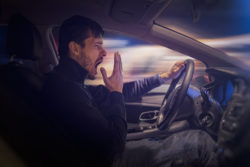 Young sleepy man is yawning and driving car at night.