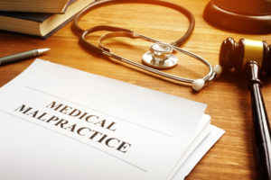 Papers labeled "Medical Malpractice" beside a stethoscope, gavel, and books on a desk.