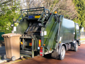 A garbage truck lifts a brown bin for emptying on a residential street.