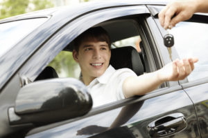 A young person in a car receives a set of keys from someone outside the vehicle.