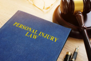 A book titled "Personal Injury Law" next to a gavel, pen, and glasses on a desk.