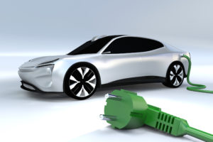 A white electric car is charging, with a green power plug in the foreground.
