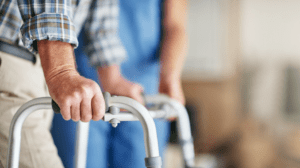 Person using a walker with assistance from a caregiver in a blue uniform.