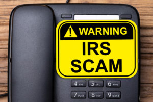 Yellow warning sign reading "IRS Scam" placed on a black desk phone.