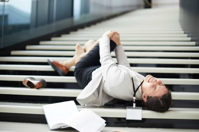 Woman lying on her back on staircase and holding knee after slip and fall injury 