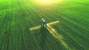A tractor sprays crops in a green field, viewed from above.