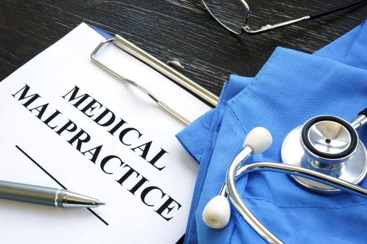 Clipboard with medical malpractice form next to a pen scrubs and stethoscope 