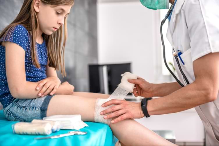Medical doctor bandaging little girls leg after child injury 