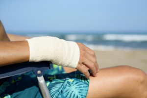 Person with a bandaged wrist sitting on a beach chair by the sea.