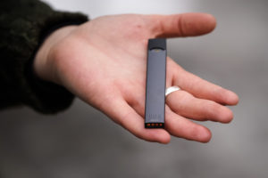 A hand holding a black vape pen with metallic contacts visible at one end.