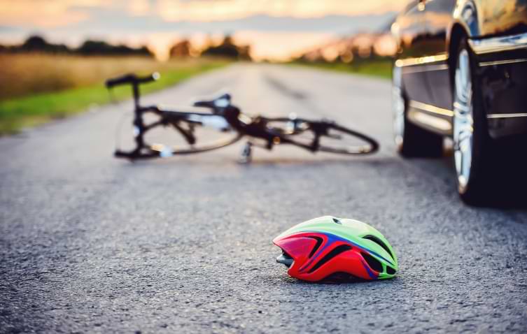 bike and helmet laying on road next to a car after a bike accident 