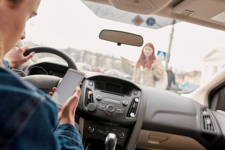 Distracted male driver looking at mobile phone about to hit a pedestrian crossing street