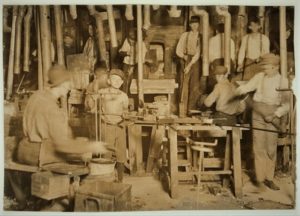 Several workers operate machinery and tools in a busy industrial workshop or factory setting.