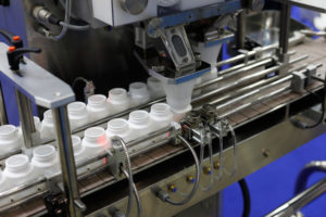 Automated machine fills plastic bottles on a production line in a factory.