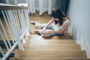 Woman sitting on wooden stairs holding her knee, appearing to be in pain.