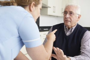 A nurse points at an elderly man who looks distressed and raises his hand defensively.