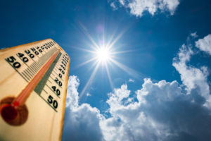 Thermometer showing high temperature under a bright sun with scattered clouds in the sky.