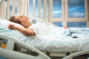 Woman lying in a hospital bed, looking upward, with medical equipment nearby.