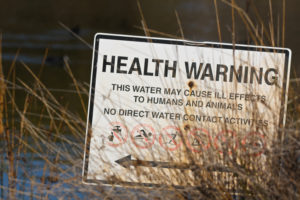 A health warning sign prohibiting water contact due to potential ill effects for humans and animals.