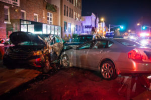 Two cars with heavy front-end damage after a nighttime collision on a city street.