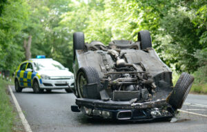 Overturned car on a road with a police vehicle parked in the background.