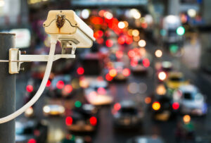 Security camera overlooking a busy city street with heavy traffic and blurred lights at night.