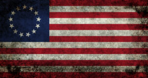 A weathered Betsy Ross flag with 13 stars in a circle and 13 red and white stripes.