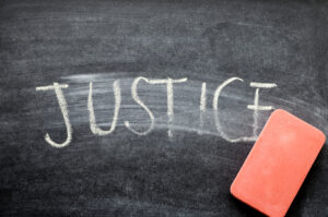 The word "justice" partially erased on a chalkboard, hinting at HR 1215 with a pink eraser.