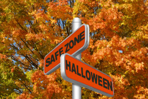 Two orange street signs read "Safe Zone" and promote Halloween Safety amid autumn trees.