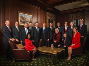 Fifteen people in business attire pose together in a formal, wood-paneled office setting.
