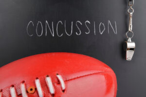 Red football and whistle on black surface, "Concussion" in chalk—CTE denial by Jerry Jones looms.