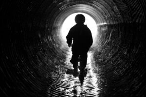 A child walks through a tunnel toward a bright light at the tunnel’s end.