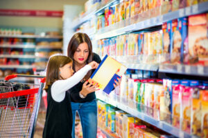 A woman and girl read a cereal box together in a grocery store aisle.