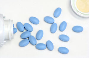 Several blue oval pills spilled from a white bottle onto a white surface.