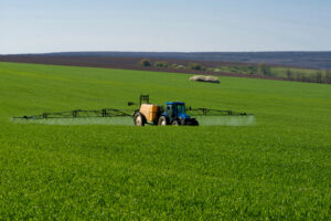 Tractor spraying pesticide across a large green field on a clear day.