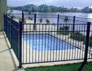 Small fenced-in swimming pool with a lake and houses visible in the background.