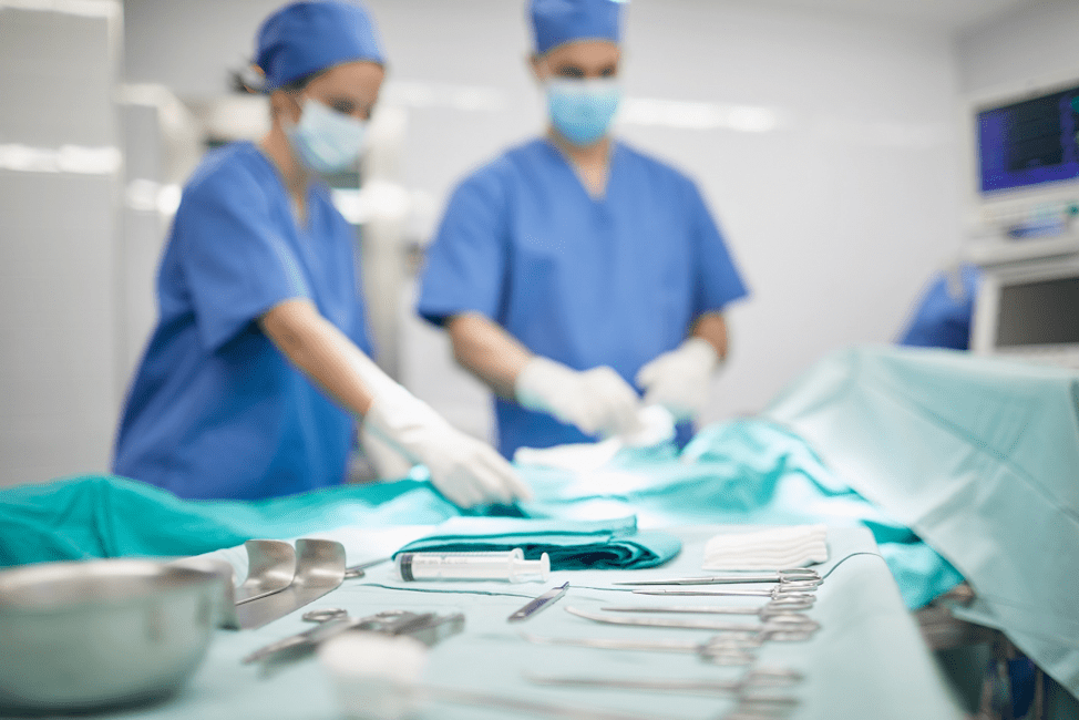 Two surgeons in scrubs perform an operation with surgical tools laid out in the foreground.