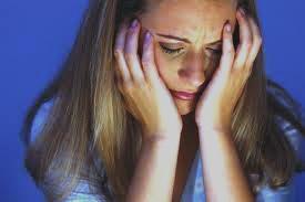 Woman holding her face in her hands, appearing upset or distressed against a blue background.